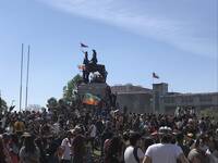 Manifestantes en Plaza Dignidad, banderas mapuche y chilena en el monumento